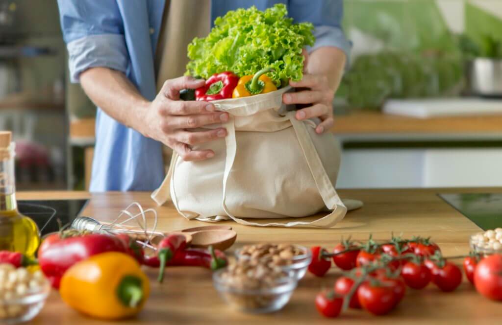Young unrecognizable man bring up full bag with fresh vegetables.